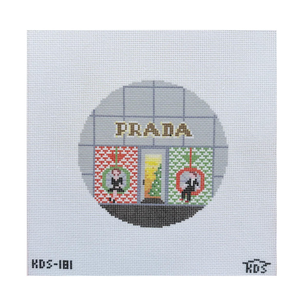 A square needlepoint canvas featuring a circular design of a Prada storefront with the brand name 'PRADA' stitched across the top. The windows show red and green patterned panels with a small Christmas tree in the center.