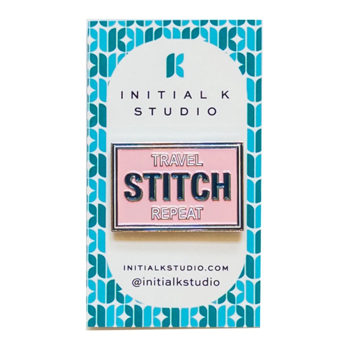 A rectangular enamel pin on a branded backing card. The pin has a pink background with navy and white text reading 'TRAVEL STITCH REPEAT.