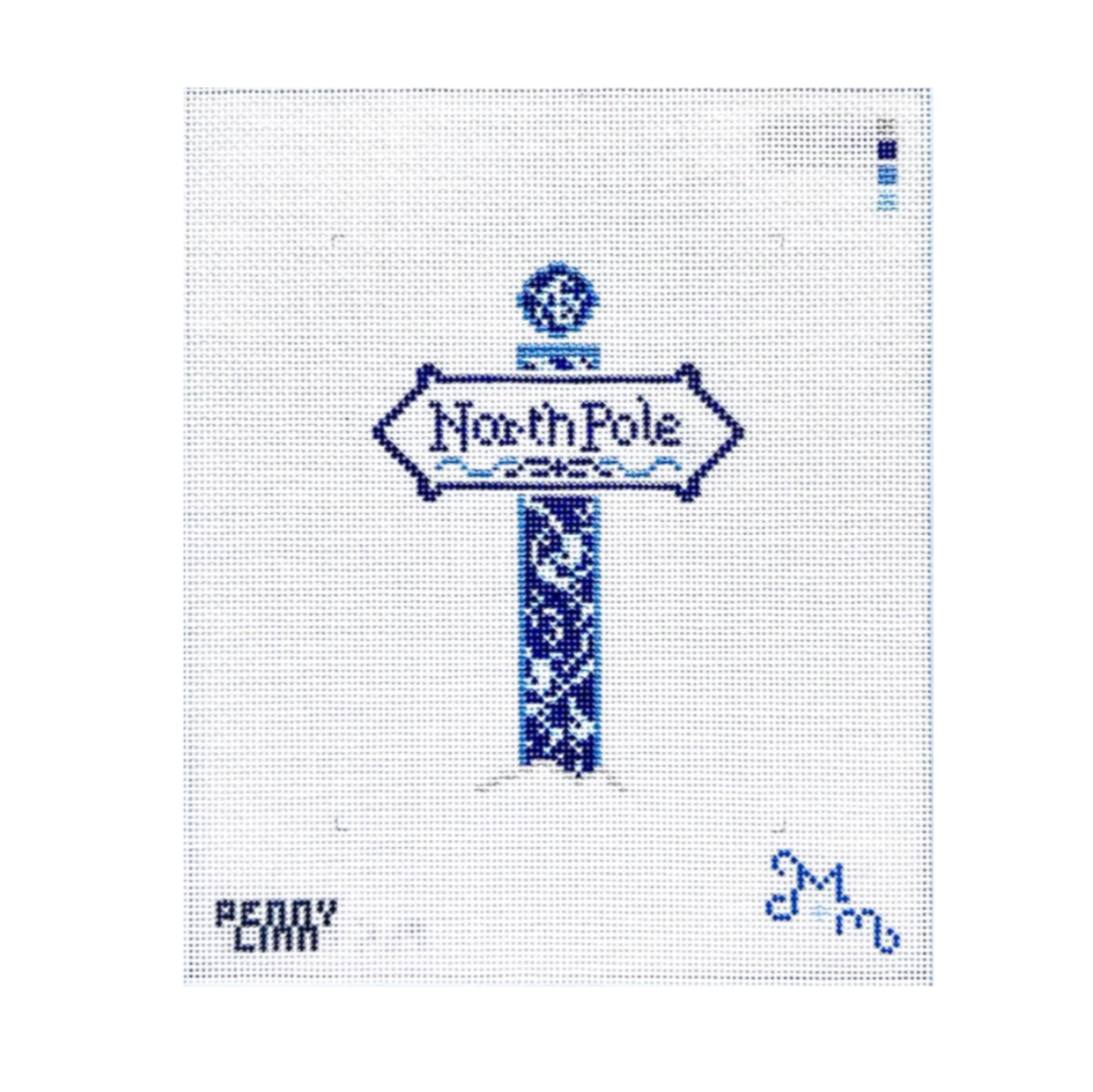 A needlepoint canvas featuring a blue and white stitched design of a 'North Pole' sign, with 'PENNY CARR' and a blue signature in the bottom corners on a white grid background.