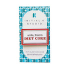 An enamel pin reading 'smile, there's DIET COKE' in red and gray lettering, mounted on a white card with a blue geometric pattern. The card is branded 'INITIAL K STUDIO'.