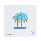 A needlepoint canvas design featuring a white basket with blue handles and a blue base, filled with light blue hydrangea flowers and green leaves. The text 'WM-ET-127' is printed in black at the bottom left, and a blue circular logo is at the bottom right, all on a white grid canvas background.