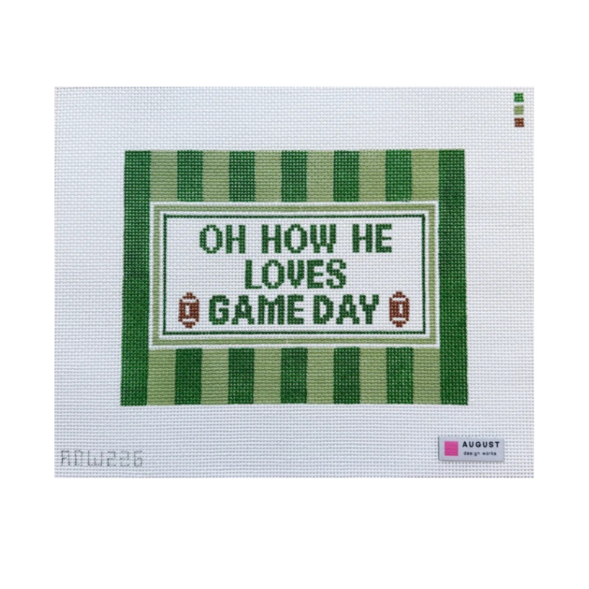 A cross-stitch needlework canvas featuring the text 'OH HOW HE LOVES GAME DAY' in green and white, framed by green and white stripes with small football motifs. The canvas is displayed flat against a white background with an August Needleworks label visible in the bottom right corner.