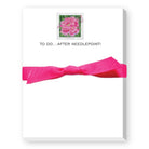 A white notepad or card with a bright pink ribbon tied around the middle and a small framed pink flower illustration near the top, with the text 'TO DO.