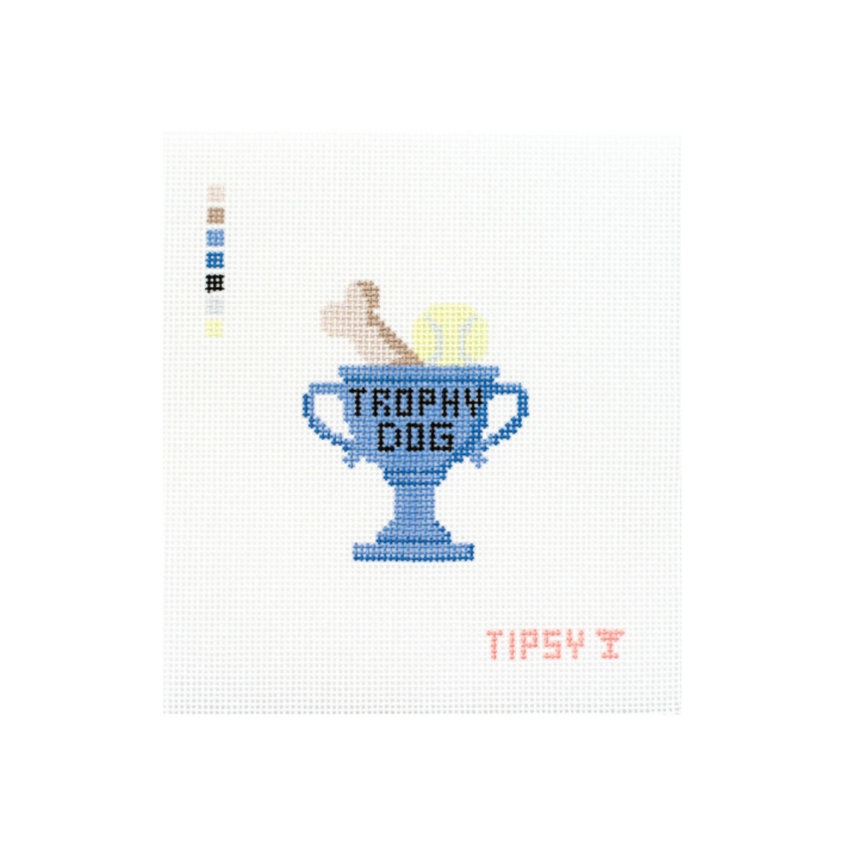 A cross-stitch style design on a white fabric background featuring a blue trophy cup with the words 'TROPHY DOG' in black, a tan dog figure climbing out of the cup, a yellow ball, and small pink text reading 'TIPSY T' below. A vertical color swatch strip appears on the left side.