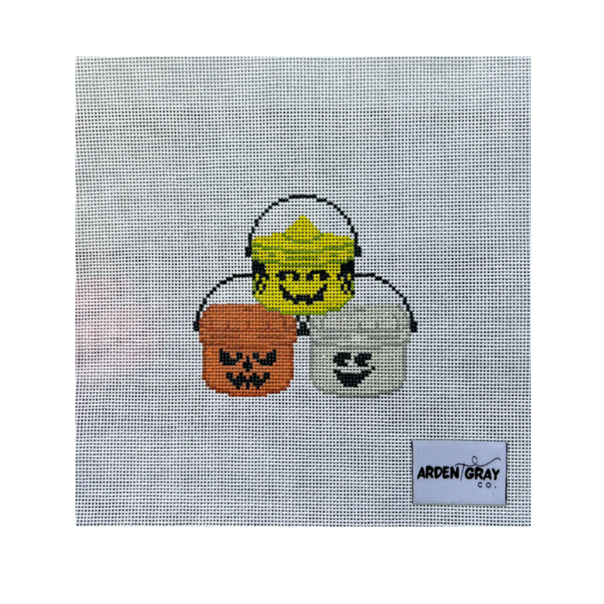 A needlepoint canvas featuring three Halloween buckets: a yellow bucket with a smiling face, an orange bucket with a pumpkin face, and a white bucket with a ghost face. The canvas has a visible 'ARDEN GRAY CO.